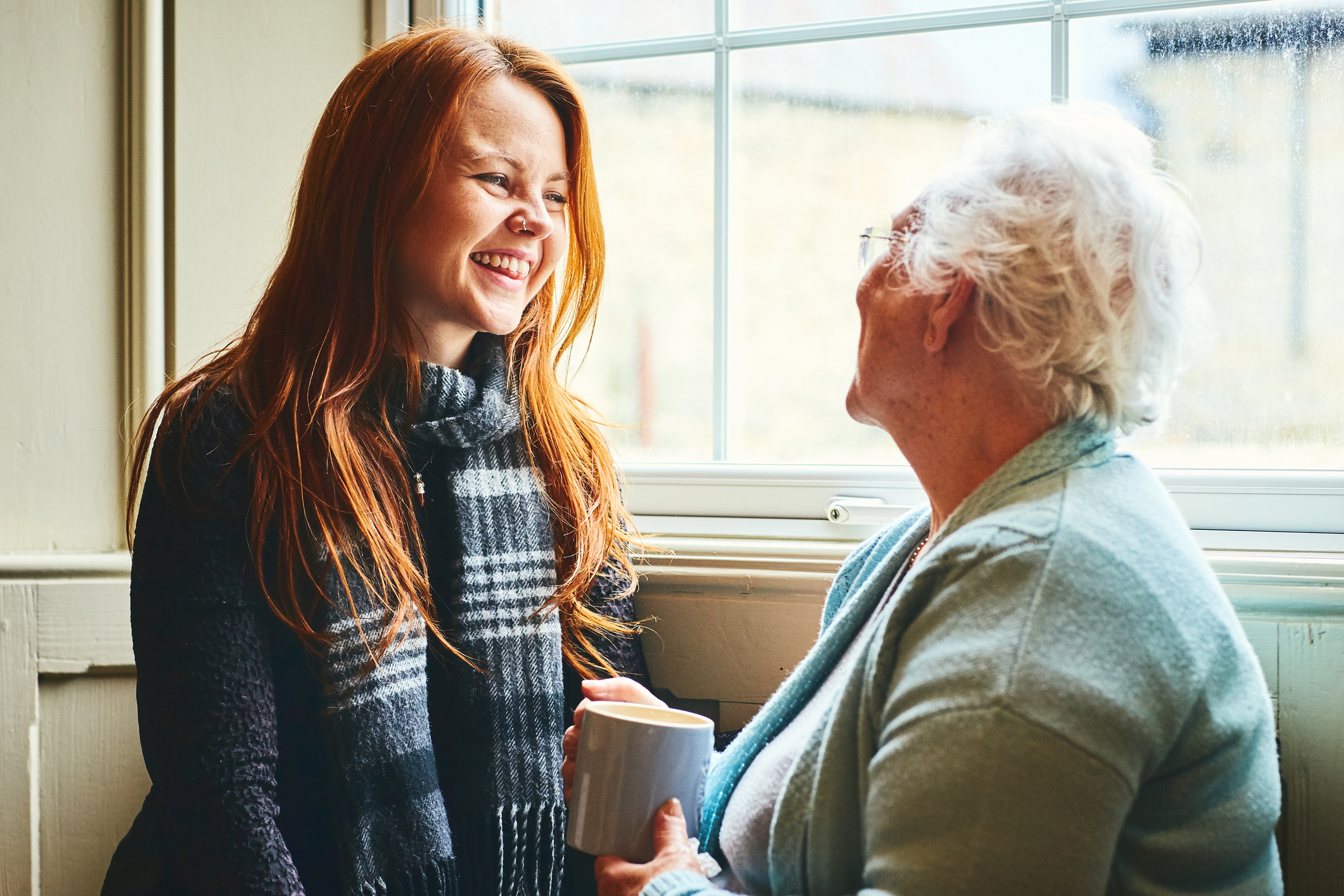 Young caregiver talks to senior woman about elderly home care solutions.