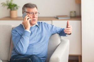 An older man answers the phone and remains vigilant for AI imposter scams against the elderly.